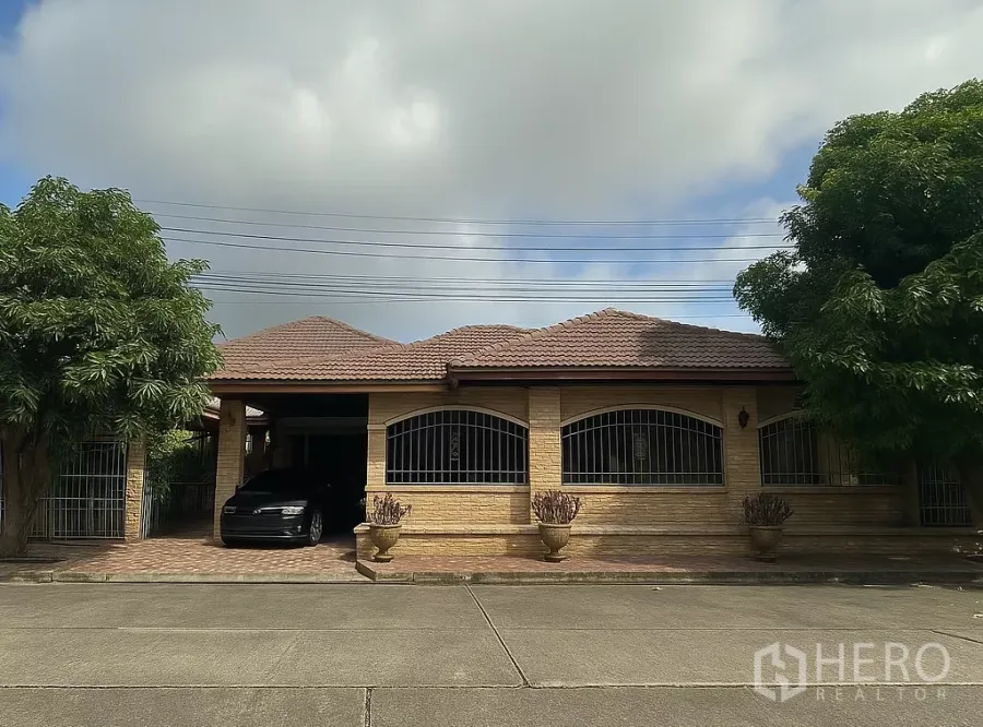 Detached House for sale in Pathum Thani - Single-storey detached brick house with tiled roof, gated windows and a front driveway carport.