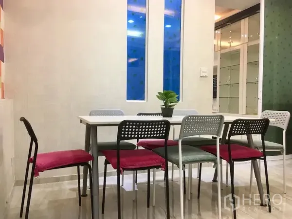 Townhouse for rent in Bang Rak, Bangkok - Dining area with white table, colorful chairs, tall narrow windows and a glass partition.