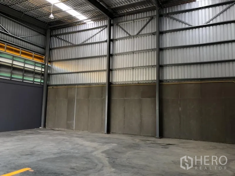 Factory for rent in Khlong Luang, Pathum Thani - Warehouse wall clad in metal sheets with skylights and smooth concrete floor.