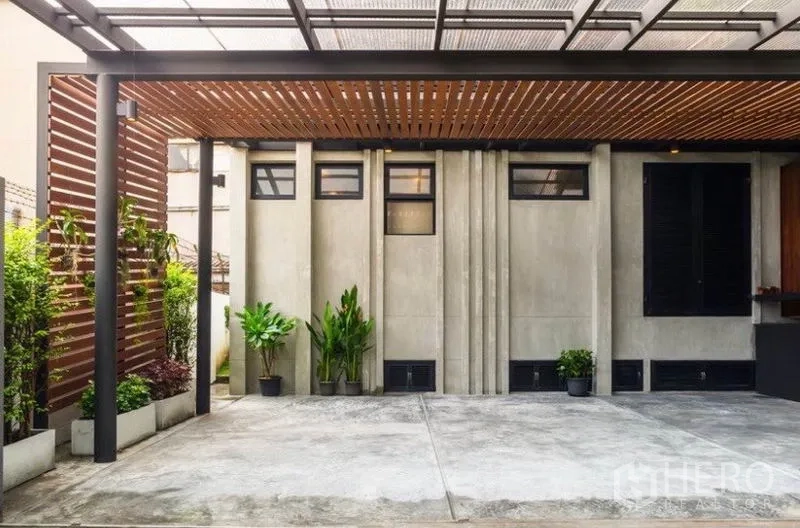 Townhouse for rent in Khlong Toei, Bangkok - Covered carport with wood slat canopy, concrete walls and potted greenery.