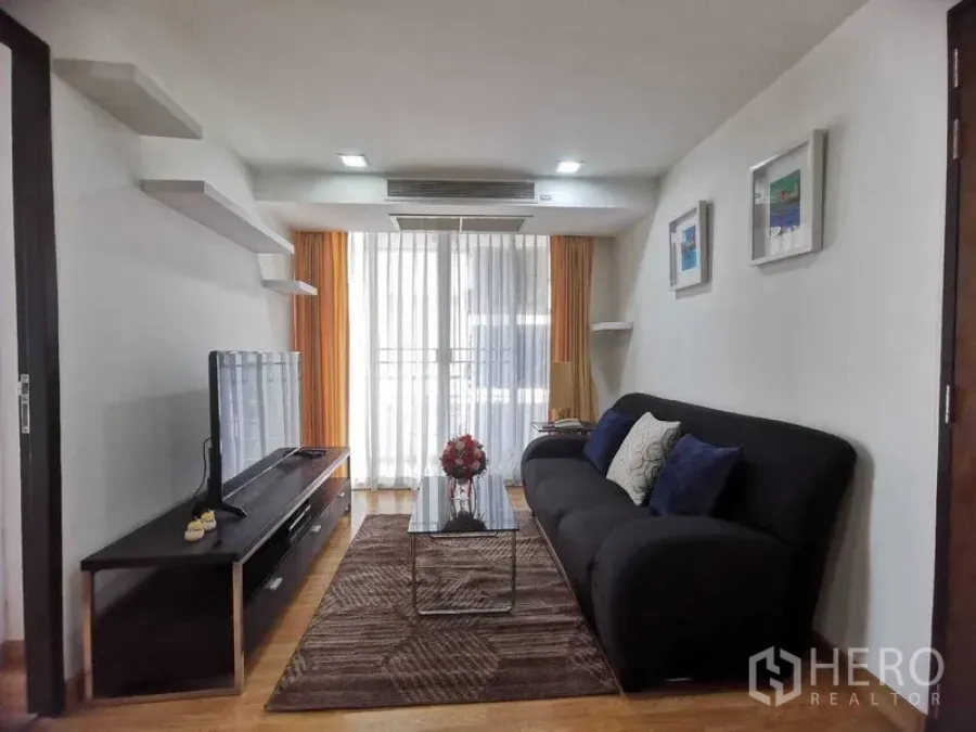 Condominium for rent in Watthana, Bangkok - Living room with dark sofa, coffee table, TV cabinet and balcony doors with sheer curtains.