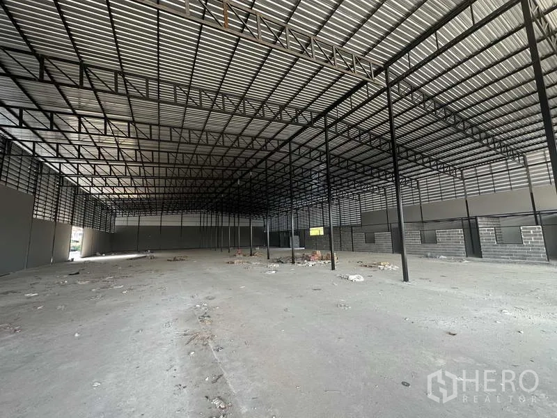 Warehouse for rent in Lam Luk Ka, Pathum Thani - Deep interior perspective with high roof, steel grid structure and service block along one wall.