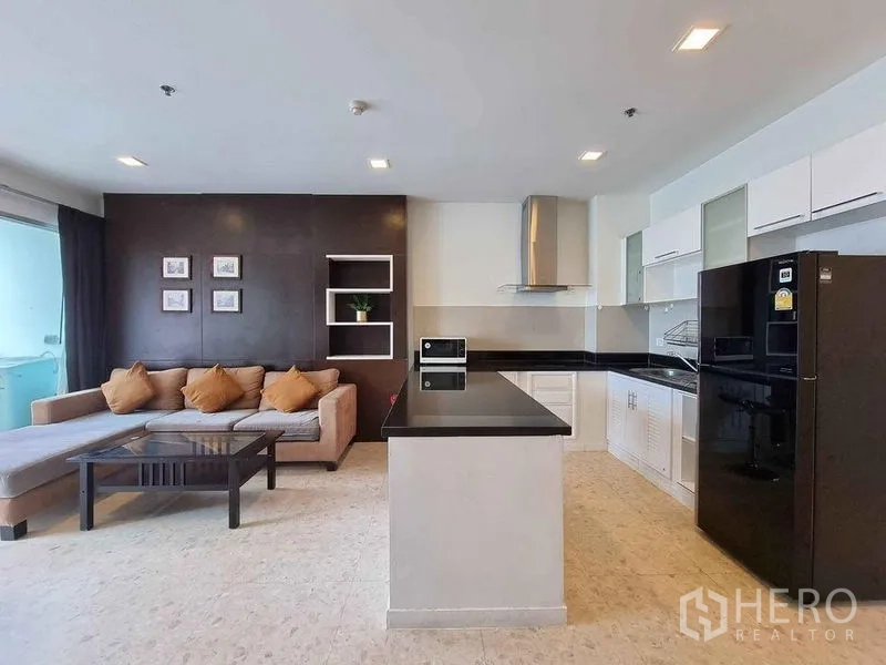 Condominium for rent in Khlong Luang, Pathum Thani - Open‑plan living and kitchen with island, black countertops and sectional sofa.