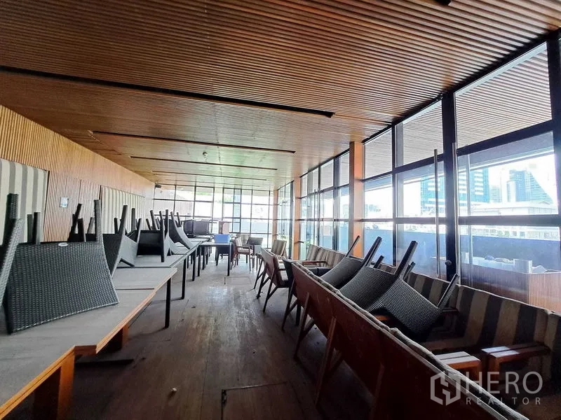 Retail Space for rent in Khlong Toei, Bangkok - Long open-plan room with wood ceiling and glass walls, stacked furniture and city outlook.