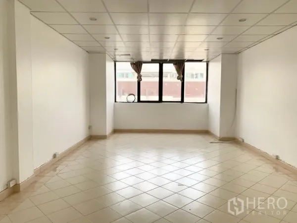 Townhouse for rent in Khlong Toei, Bangkok - Spacious living area with white walls, tiled floor, recessed ceiling lights, and a wide window.