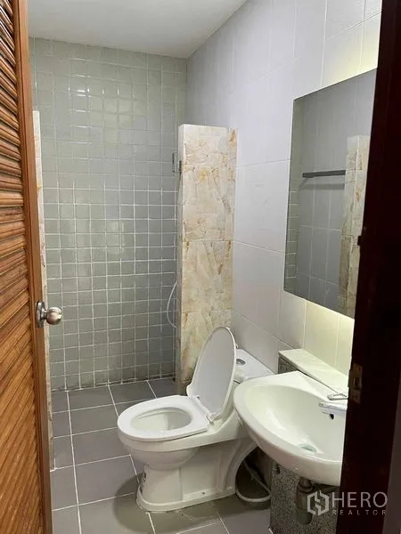 Home Office for rent in Bang Kapi, Bangkok - Clean bathroom featuring a toilet, sink, mirror and tiled shower area.