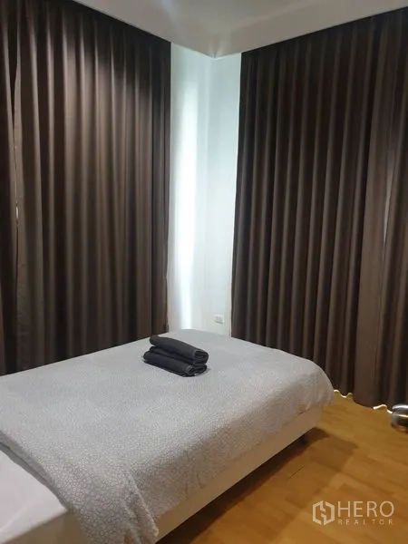 Condominium for rent in Khlong Toei, Bangkok - Second bedroom with double bed and corner windows covered by curtains.