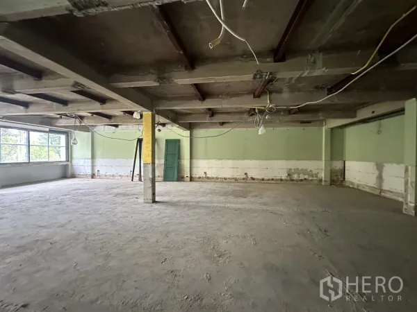 Office Space for rent in Bang Rak, Bangkok - Wide interior with structural pillars, unfinished floor and green accent wall.