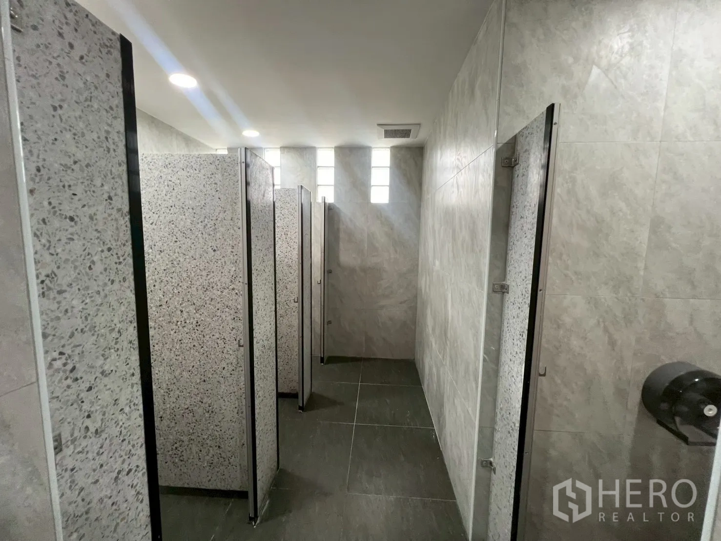 Office Space for rent in Watthana, Bangkok - Row of toilet cubicles with terrazzo partitions and ceiling lights.