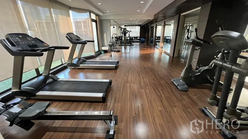 Condominium for rent in Khlong Toei, Bangkok - Condominium fitness center with treadmills, exercise bikes and floor-to-ceiling windows.