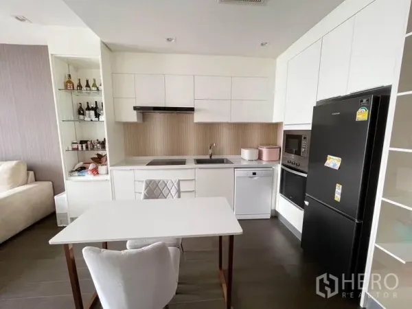 Condominium for rent in Pathum Wan, Bangkok - Modern white kitchen with cooktop, oven, dishwasher, and large black refrigerator.
