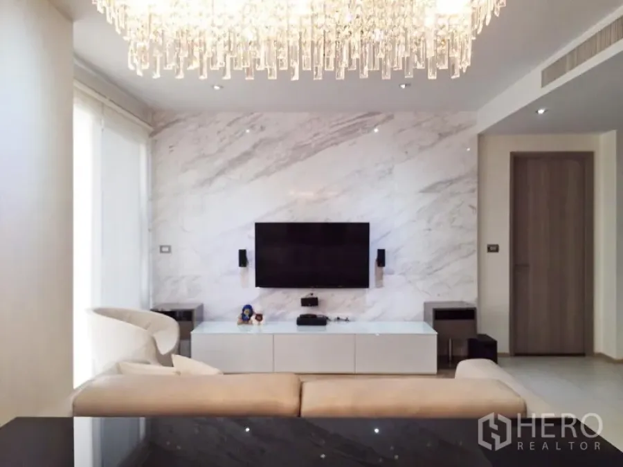 Condominium for rent or sale in Watthana, Bangkok - Bright living room with a marble feature wall, wall-mounted TV and crystal chandelier in a Thonglor condo.