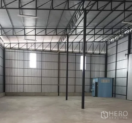 Warehouse for rent in Bueng Kum, Bangkok - Open warehouse floor with steel columns, vented windows, and a small utility room along the wall.