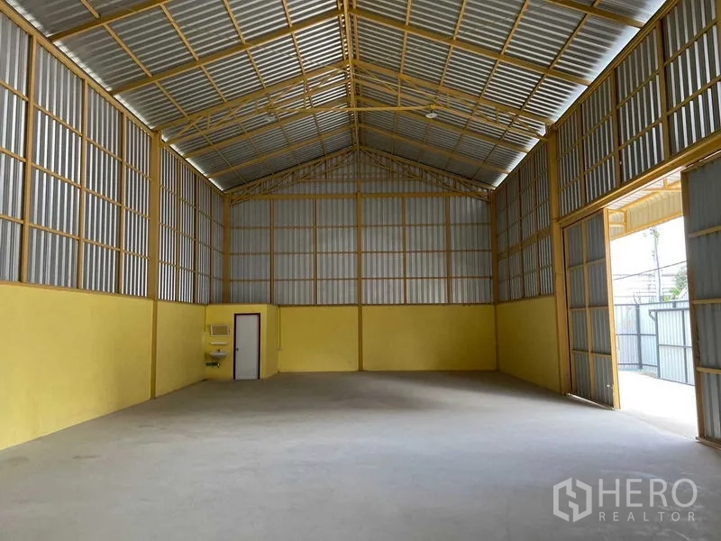 Warehouse for rent in Lat Krabang, Bangkok - Warehouse hall facing the loading door with high ceiling, small sink, and side access door.