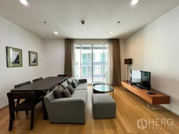 Condominium for rent in Khlong Toei, Bangkok - Open-plan living and dining room with grey sofa, long dining table and sliding doors to a balcony.