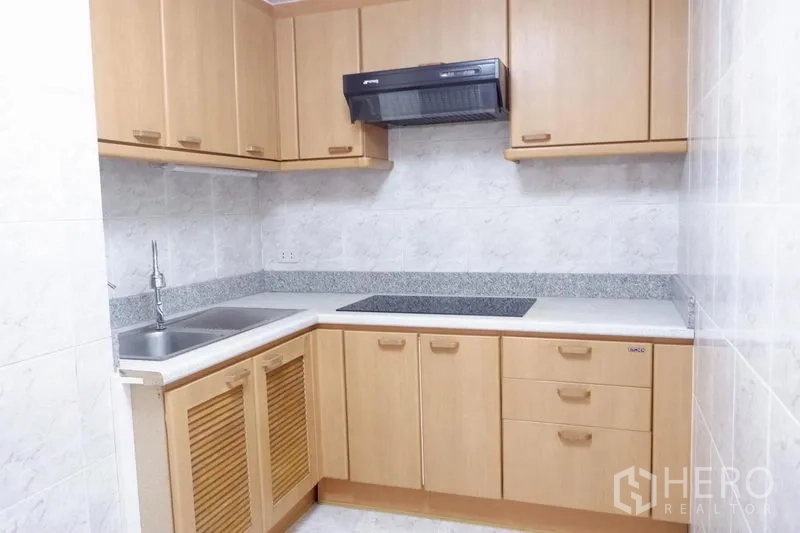 Condominium for rent in Khlong Toei, Bangkok - Enclosed kitchen with light wood cabinetry, electric cooktop, range hood and double sink.