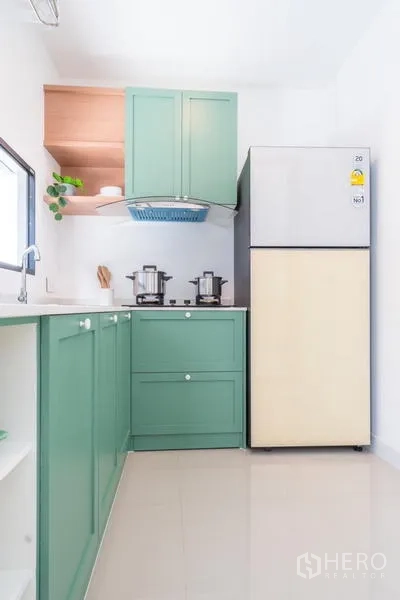 Townhouse for rent or sale in Suan Luang, Bangkok - Compact Thai kitchen with green cabinetry, corner hob, sink, and a large refrigerator.