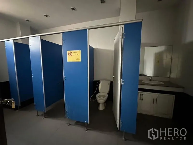 Warehouse for rent in Prawet, Bangkok - Restroom with blue partition stalls and a washbasin counter.