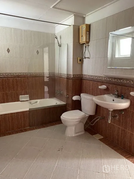 Apartment for rent in Khlong Toei, Bangkok - Bathroom with bathtub, toilet, sink, mirror and water heater on tiled walls.