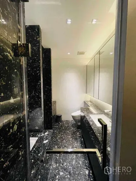 Condominium for rent in Khlong Toei, Bangkok - Luxurious bathroom with black marble finishes, large vanity and glass shower.