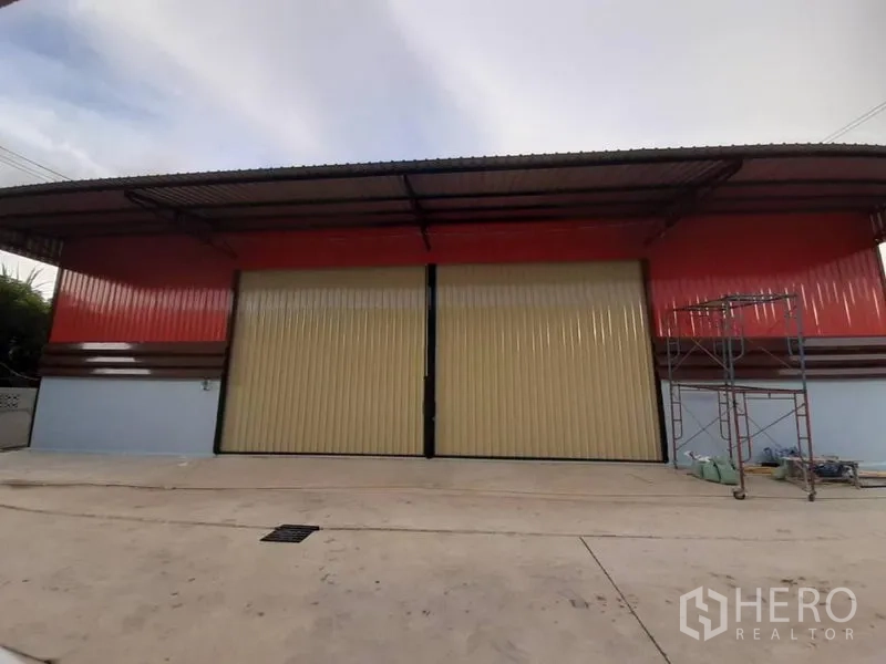 货栈 出租在Lam Luk Ka, Pathum Thani - 仓库正立面，红色墙板、米色推拉门与带顶装卸区。