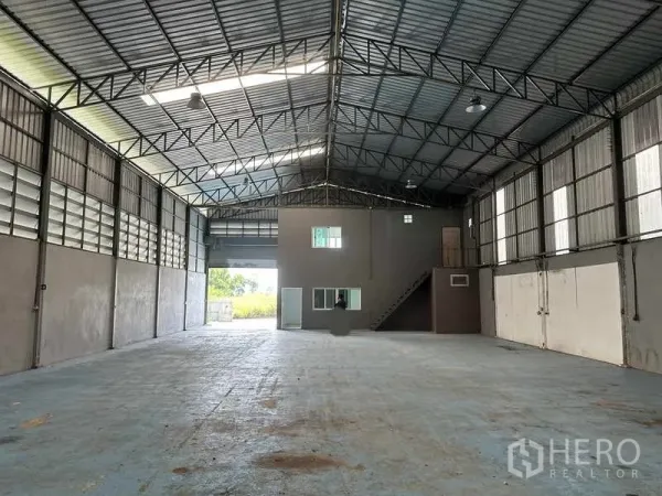 Warehouse for rent in Pathum Thani - Spacious warehouse interior with high steel truss roof, skylights and a small mezzanine office with stair.
