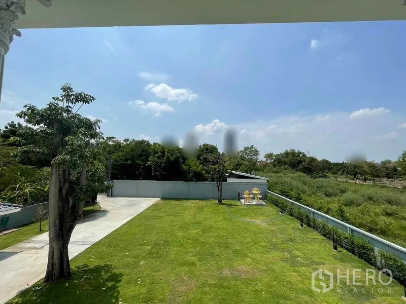 Detached House for sale in Bang Na, Bangkok - Expansive green garden and driveway bordered by mature trees and boundary wall.