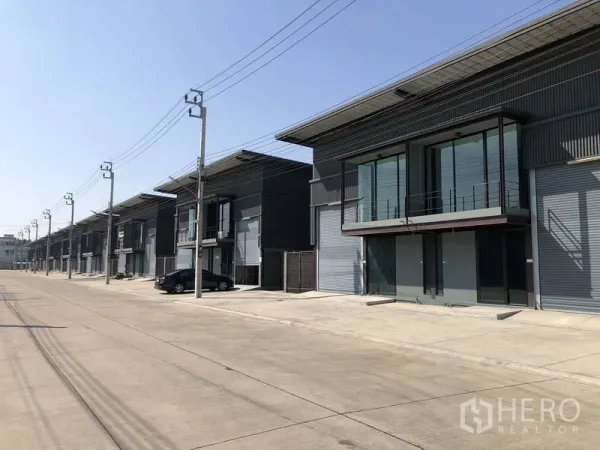 Warehouse for rent in Bang Phli, Samut Prakan - Row of new warehouses along a wide industrial road with parking and power lines.