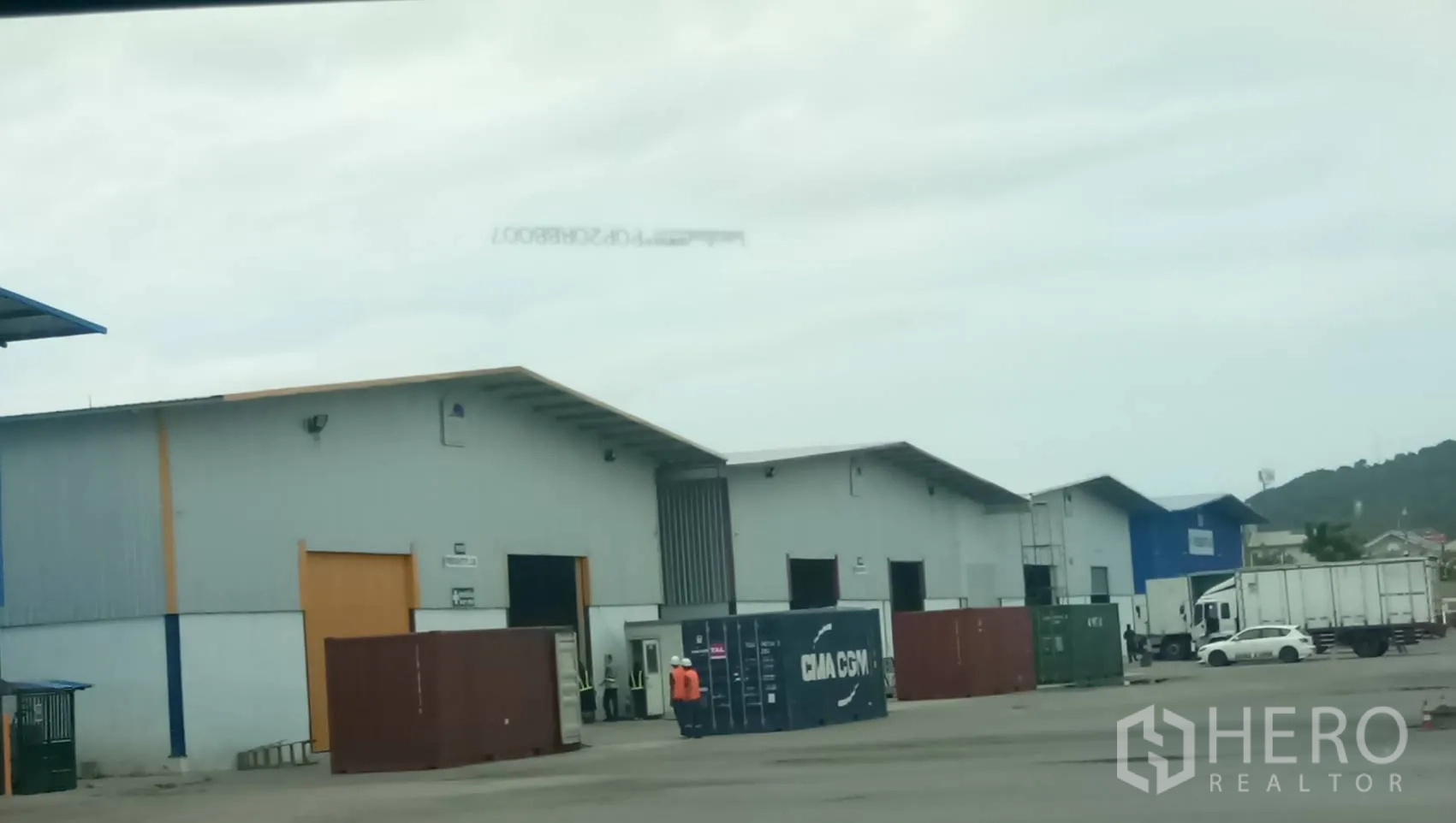 Warehouse for rent in Si Racha, Chon Buri - Row of gray warehouse buildings with shipping containers and trucks in a large yard in Si Racha.