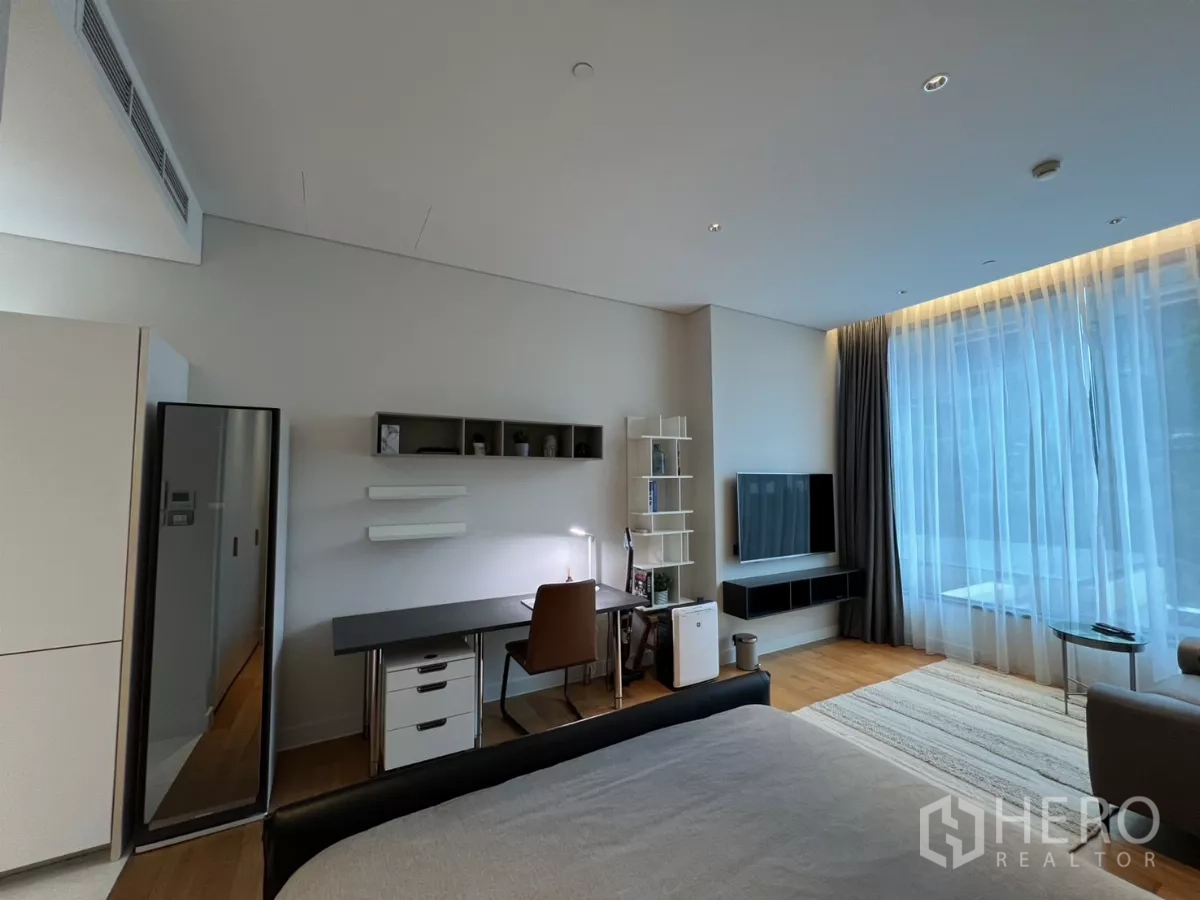 Condominium for rent in Pathum Wan, Bangkok - Wide room view showing bed, study nook, wall-mounted TV and expansive window.