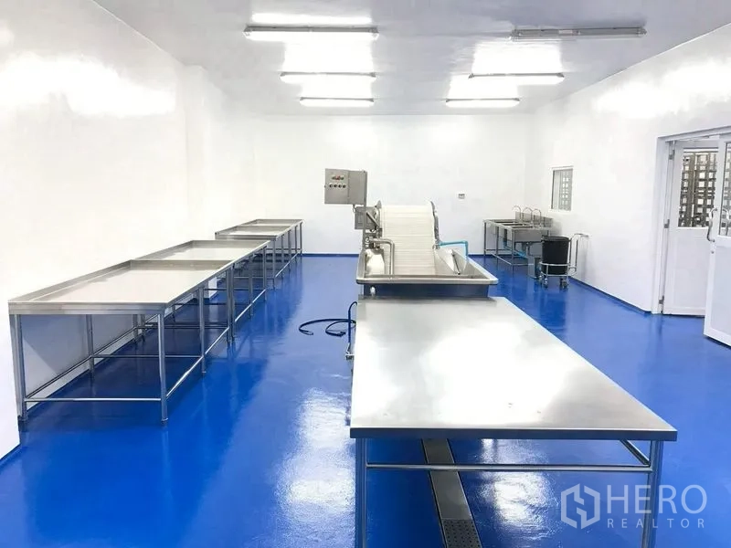 Factory for rent or sale in Krathum Baen, Samut Sakhon - Processing room with a conveyor machine and stainless benches on smooth epoxy flooring.