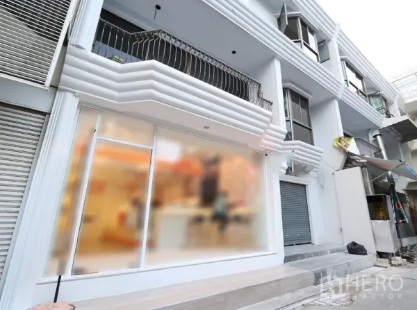 Retail Space for rent in Pathum Wan, Bangkok - Modern white shopfront with a large glass display, balcony and roller shutter on a multi-storey retail building.