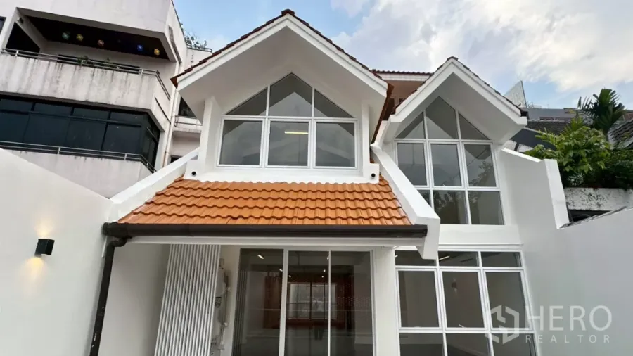 带办公室的家 出租在Watthana, Bangkok - 白色人字屋顶外立面，大片窗户与橙色瓦顶的入口。