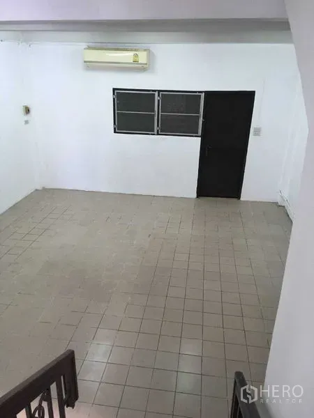 Townhouse for rent in Phra Khanong, Bangkok - Spacious tiled living area with wall-mounted air conditioner, black door and twin windows.