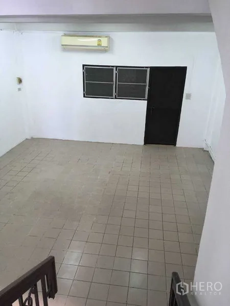 Townhouse for rent in Phra Khanong, Bangkok - Spacious tiled living area with wall-mounted air conditioner, black door and twin windows.