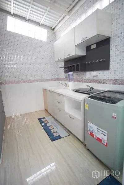 Townhouse for rent in Suan Luang, Bangkok - Bright tiled kitchen with built-in cabinets, sink and washing machine under a skylight.