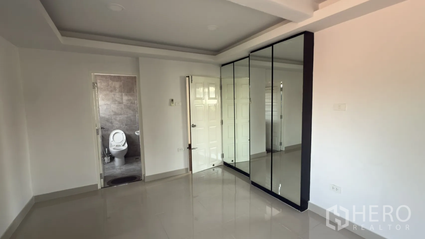 Townhouse for rent in Watthana, Bangkok - Bedroom featuring mirrored wardrobes and an ensuite bathroom finished in gray tiles.