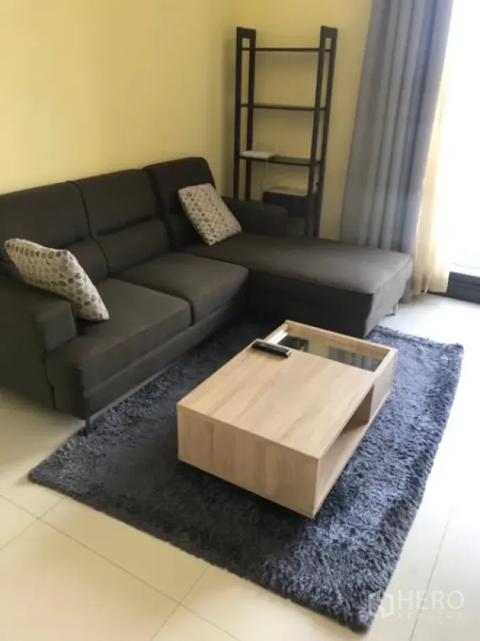 Condominium for rent or sale in Khlong Toei, Bangkok - Cozy living room with L-shaped sofa, shag rug, wooden coffee table and large window curtains.