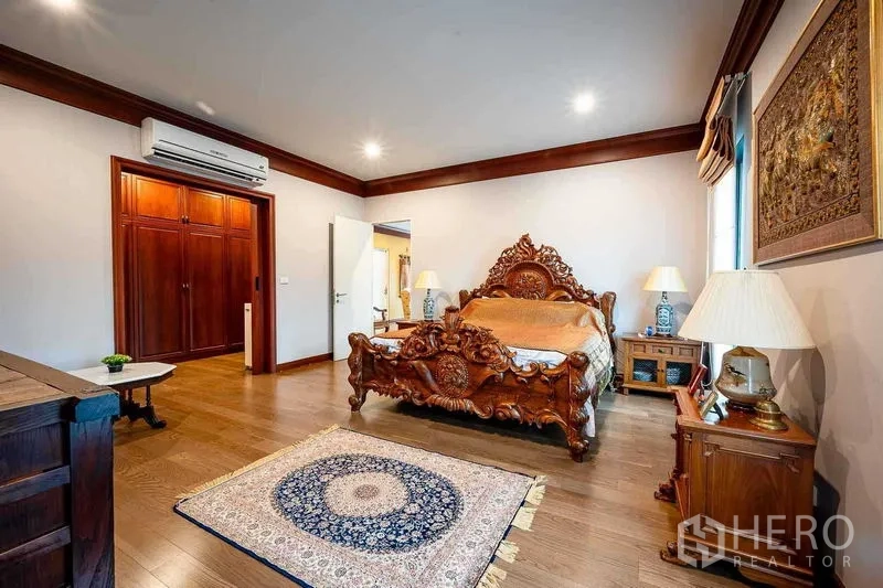 Detached House for sale in Prawet, Bangkok - Grand master bedroom with ornate carved wooden bed and built‑in wardrobe.