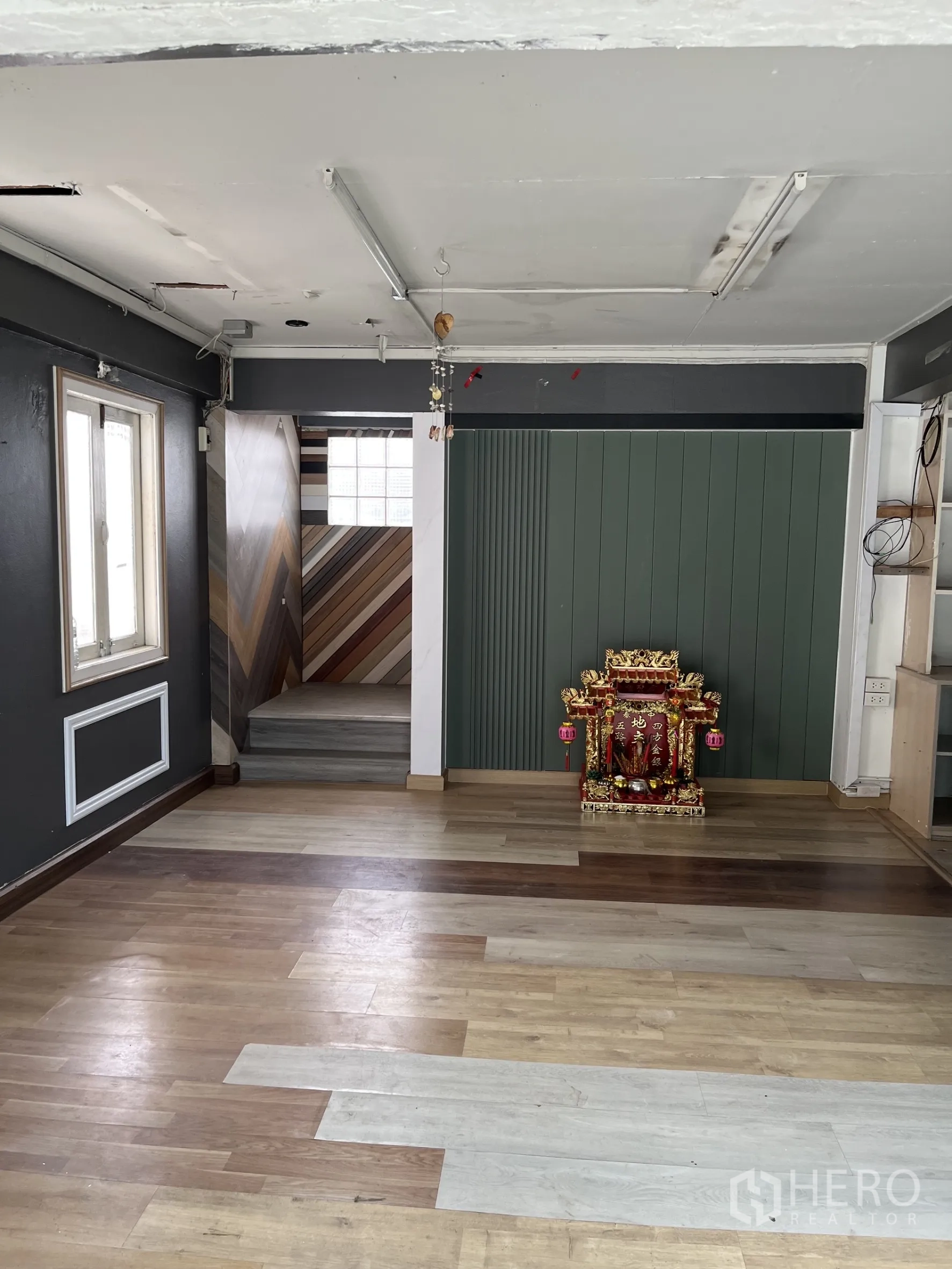 Warehouse for rent in Bangkok - Open room with mixed wood flooring, window and stairwell featuring chevron wall panels.