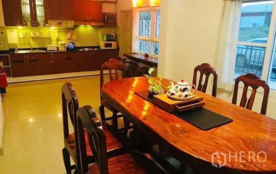 Detached House for rent or sale in Lam Luk Ka, Pathum Thani - Dining area with solid wood table adjoining a full fitted kitchen with upper and lower cabinets.