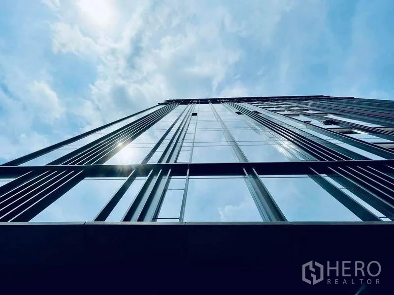 Condominium for sale in Pathum Wan, Bangkok - Upward view of a modern glass high-rise condominium facade against a blue sky.