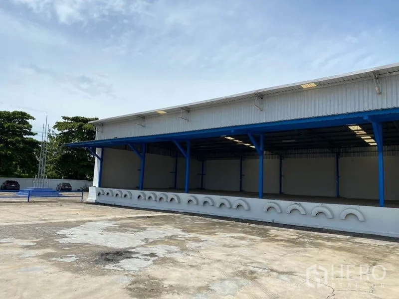 Factory for rent in Nonthaburi - Factory exterior with sheltered loading bays and an open concrete yard for trucks.