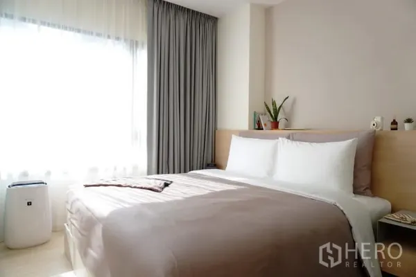 Condominium for rent in Pathum Wan, Bangkok - Light-filled bedroom with queen bed, large window, and soft grey curtains.
