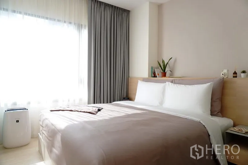 Condominium for rent in Pathum Wan, Bangkok - Light-filled bedroom with queen bed, large window, and soft grey curtains.