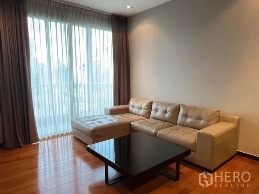 Condominium for rent - Cozy seating area with sectional sofa and coffee table by large sheer‑draped windows.