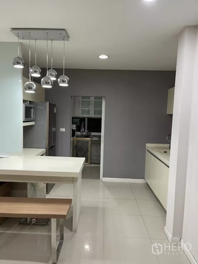 Detached House for rent in Bang Kapi, Bangkok - Kitchen area with island, grey accent wall and doorway to secondary kitchen.