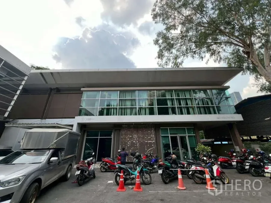 Office Space for rent in Watthana, Bangkok - Two-storey office building with glass facade and motorcycles parked out front under a wide roof eave.