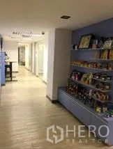 办公空间 出租在Khlong Toei, Bangkok - 走廊设展示货架，旁为玻璃会议室与浅色木地板。
