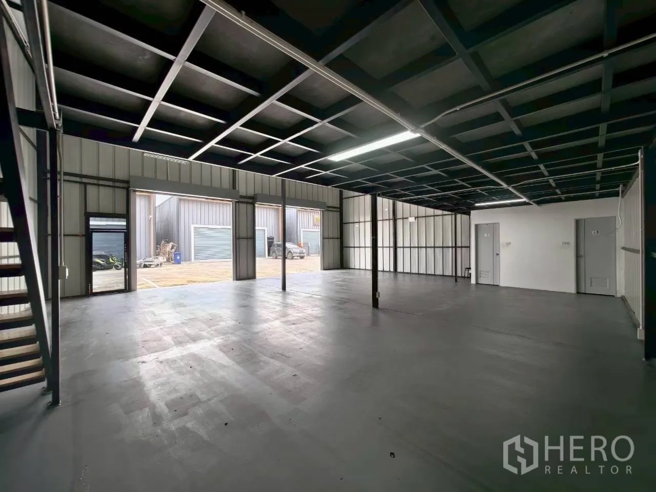 Warehouse for rent in Suan Luang, Bangkok - View from under the mezzanine showing multiple roller shutters, steel columns, and two utility doors.
